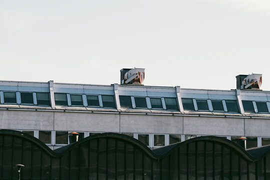 Rooftop windows line an industrial building above arches, where ventilation panels and overcast architecture shape the facade elevation