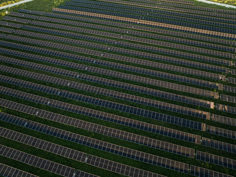 Aerial view of rows of solar panels in a large photovoltaic power plant surrounded by green grass in Augusta, Sicily, Italy.