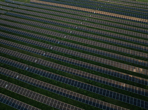 Aerial view of a large solar panel farm with long diagonal rows of photovoltaic modules installed on green grass Augusta, Sicily, Italy.