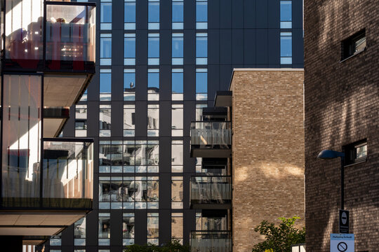 Apartment balcony fronts a glass office facade in Loren where urban architecture layers residential and business buildings in Oslo, Norway