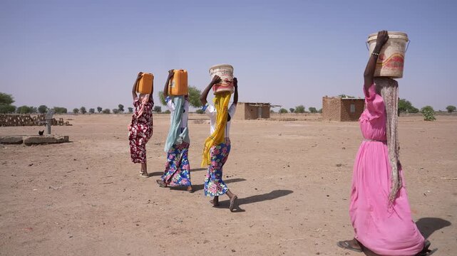 African women walking with water containers in dry village, April 25, 2026, Chad, N Djamena