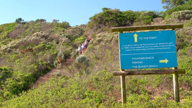 Direction signage with hikers hiking through coastal vegetation on Robberg trail