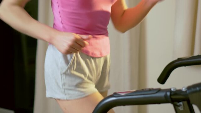 Dynamic stride of unrecognizable female body on treadmill during indoor cardio workout. Continuous jogging movement reflecting endurance training and consistent home fitness routine. Active healthy