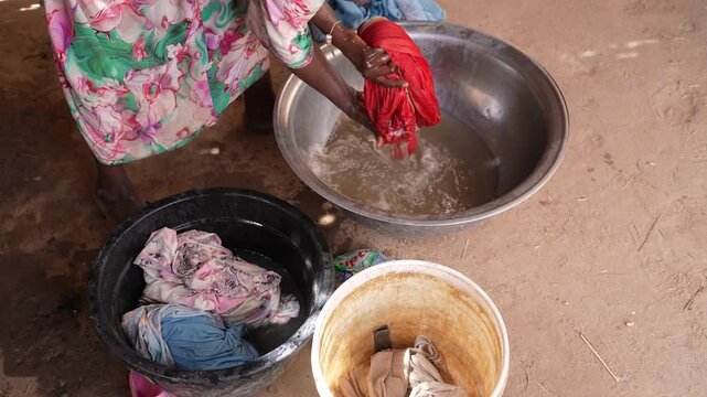 African woman rinsing washed clothes beside basin at home, April 25, 2026, Chad, N Djamena
