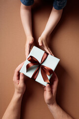 Child's hands giving Father's Day gift box to dad on brown background
