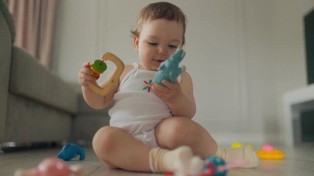 Early growth as infant girl plays with rhino and wooden rattle on floor