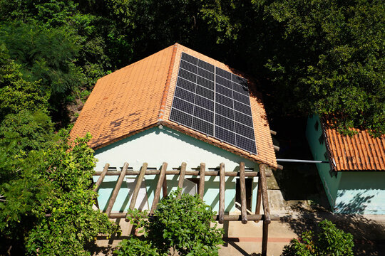 Aerial View of a Sustainable Eco-Friendly House with Solar Panels on an Orange Clay Tile Roof Surrounded by Lush Green Trees