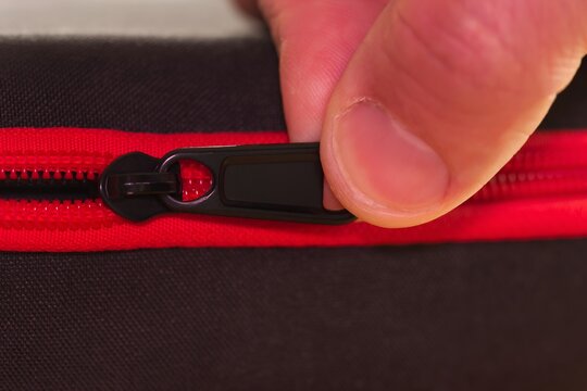 Fingers are pushing the red zipper on the bag.