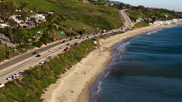Pacific Coast Highway traffic along the Malibu coastline, the drone moving in parallel with cars on California's most scenic coastal route.