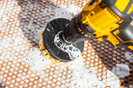 Yellow electric drill with brush attachment scrubbing hexagonal tile floor with soap foam. Concept for professional cleaning and home maintenance.