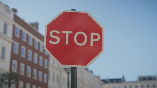cinematic close-up shot of a classic London stop sign on a quiet upscale street. Shallow depth of field with soft blurred London architecture in the background, moody overcast lighting, subtle rain re