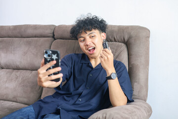 Fototapeta premium Young Asian Man Taking Selfie Holding Vape Device On Sofa