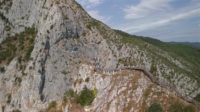 Aerial pull-back shot revealing the wooden spiral observation deck at Valla Canyon with tourists, Turkey.