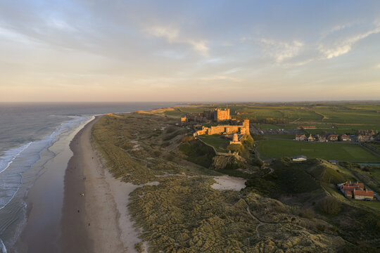 Aerial view of Bamburgh Castle overlooking the sandy beach and North Sea coastline during golden hour in Bamburgh, England, United Kingdom.