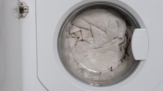 Washing machine cycle in action showing clothes tumbling inside glass door. Household laundry appliance cleaning textile items during home maintenance routine task.