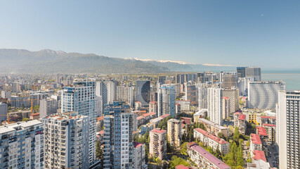 Naklejka premium Batumi skyline with modern high-rise buildings, Black Sea coast and Caucasus mountains under clear blue sky, Georgia travel cityscape