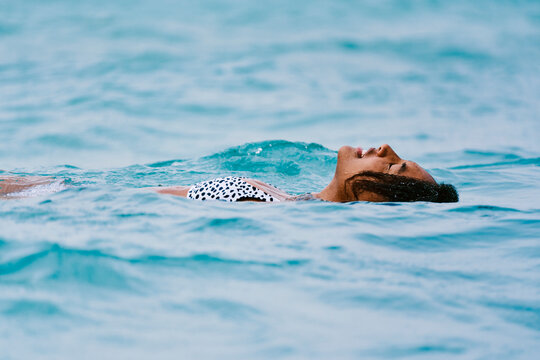A serene woman floats peacefully on her back in the calm blue ocean water. She wears a patterned swimsuit, enjoying a moment of relaxation and tranquility.