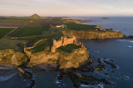 Aerial view of Tantallon Castle on a rocky cliff overlooking the North Sea with green fields and North Berwick Law in the distance during golden hour North Berwick, Scotland, United Kingdom.