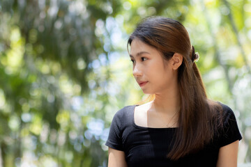 Fototapeta premium Young asian woman portrait looking away standing outdoor in nature park feeling thoughtful and peaceful enjoying fresh natural summer sunlight environment with blurred green tree leaf background