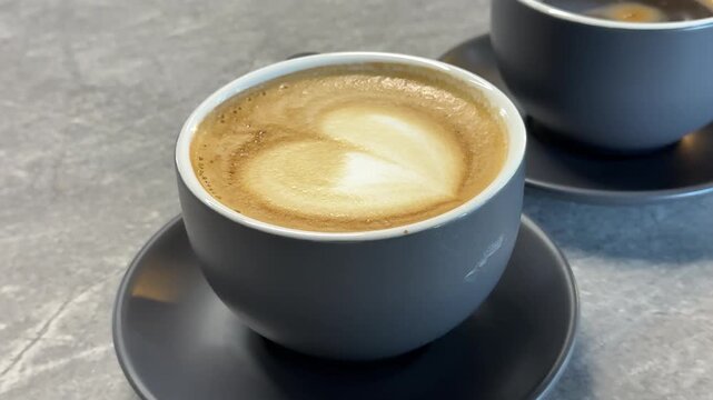 Two gray coffee cups on saucers with latte art heart and espresso shot, cozy cafe morning atmosphere, aesthetic beverage concept, warm minimal coffee culture scene
