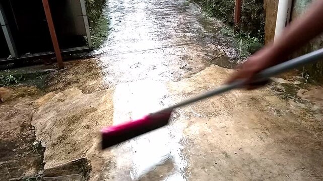 Person sweeping rainwater with pink squeegee on outdoor concrete path