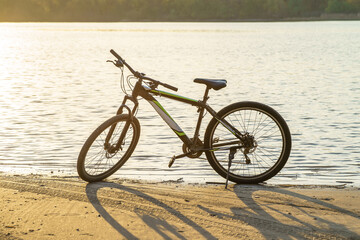 Fototapeta premium A bicycle parked on the riverbank, with sunlight reflecting off the water surface.