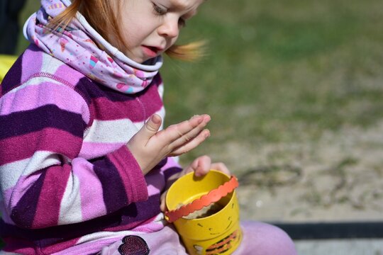 Toddler girl examining sand on her hands while playing in a sunny playground sandbox, enjoying sensory outdoor activities and creative childhood exploration.