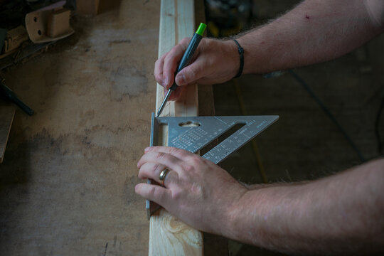 Close-up of carpenter marking timber using a speed square and pencil, showing precision layout work in woodworking and construction.