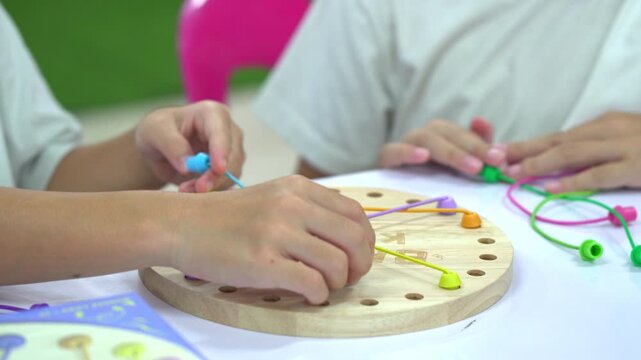 Close up of children's hands playing with a colorful wooden stringing toy, practicing fine motor skills and hand-eye coordination.