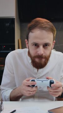 Attractive young man playing video game in moderm kitchen apartment enjoying indoor activity. Online entertainment and leisure activity concept.