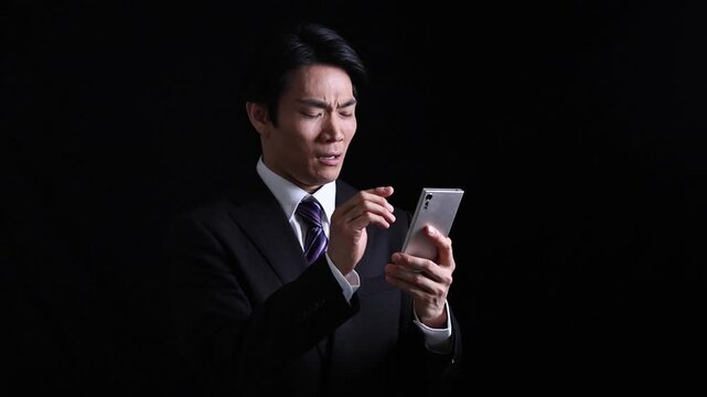 スマートフォンで悲しい知らせを受けて落ち込むビジネスマン 黒背景