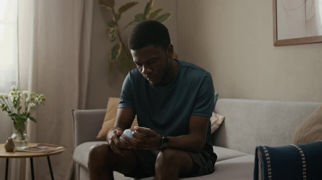 Young adult African American man checking CGM applicator for proper sensor placement while sitting on couch in living room, diabetes wellness routine