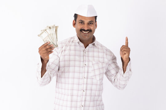 Portrait of young indian marathi man wearing white topi showing indian rupees against white background