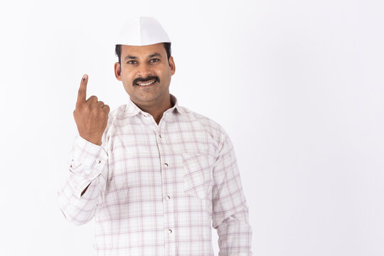 Portrait of a mid aged indian man in topi showing vote finger against white studio background