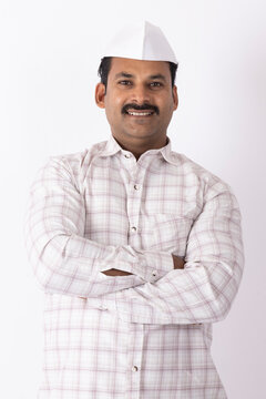 Portrait of smiling young indian farmer or rural man wearing topi looking at camera while standing on white background