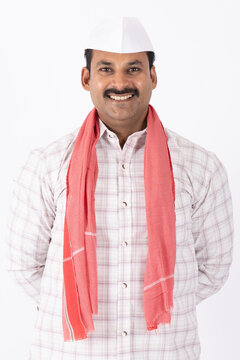 Portrait of smiling young indian farmer or rural man wearing topi looking at camera while standing on white background