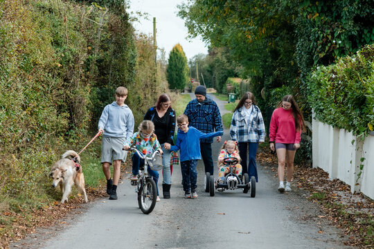 Girl with ponytails riding a toy car with her family and dog walking behind her