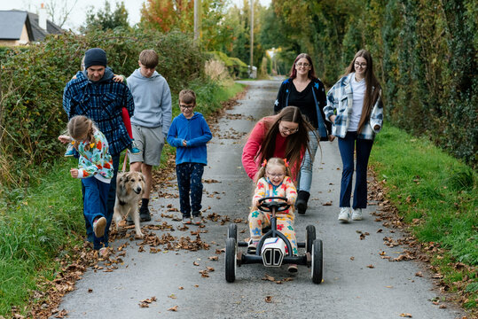 Girl with ponytails riding a toy car with her family walking behind her