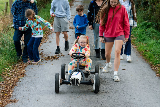 Girl with ponytails riding a toy car with her family walking behind her