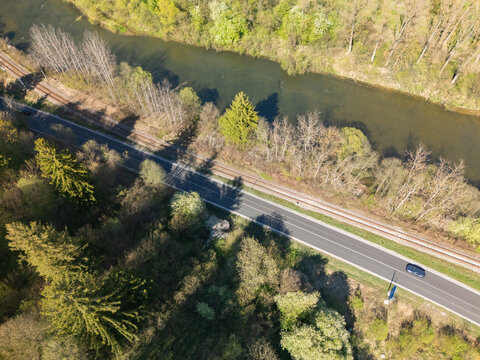 Aerial view of the Orava river flowing alongside a railway track and a road with a car passing through lush green forests Nizna, Zilina Region, Slovakia.