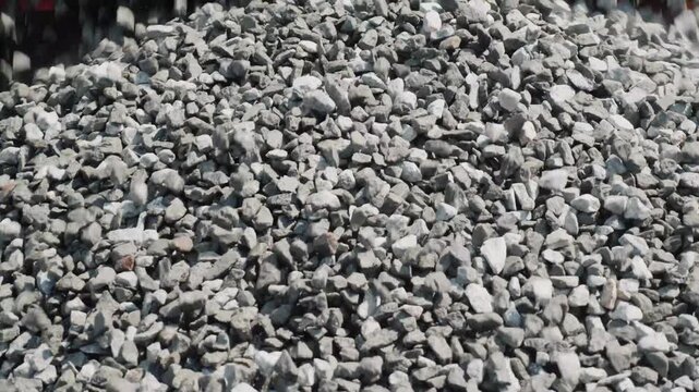 A close-up view of crushed stones, gravel, and small rocks falling from above, forming a large heap of construction material.