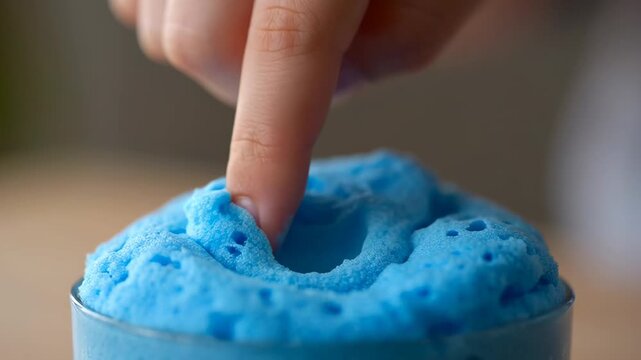 Finger pressing into blue foam in a glass. Close up of a scientific experiment.