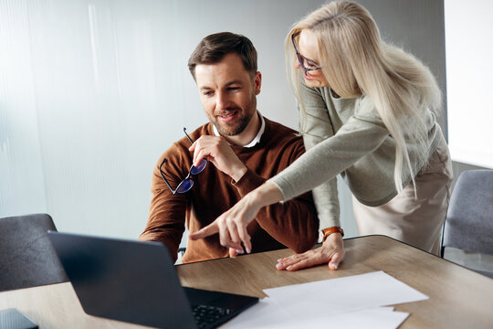Business executive pointing on laptop screen while collaborating with male colleague in a modern office discussion