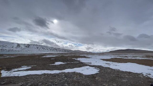 A cinematic 4K time-lapse capturing fast-moving dark clouds over a vast snowy plateau and distant mountains in Xizang China.