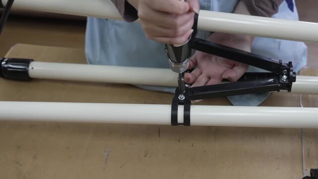 Close-up of worker attaching black tube ring clamp bracket to white telescope tripod leg using power drill