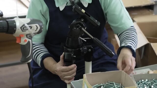 Worker assembling telescope tripod by attaching white legs to black equatorial mount head with hand tools