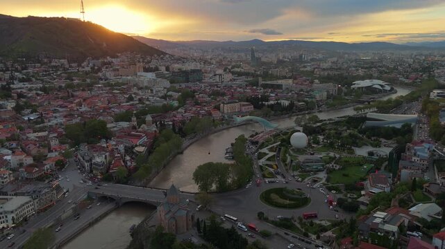 Tbilisi aerial sunset view with Bridge of Peace, Mtkvari River, and Public Service Hall. Cityscape of Georgia's capital featuring Rike Park, Metekhi Church, and the historic Old Town at golden hour