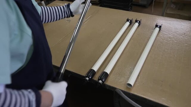 Worker in apron arranging white painted telescope tripod legs on cardboard surface in warehouse area