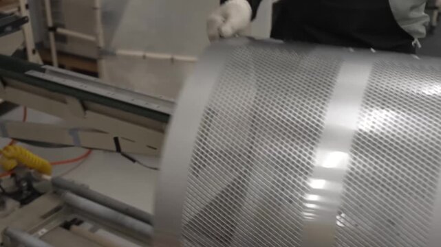 Factory worker carrying completed perforated stainless steel washing machine inner drum to storage area