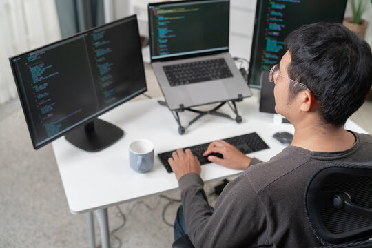 Software Developer Working at Desk with Multiple Computer Monitors Showing Programming Code